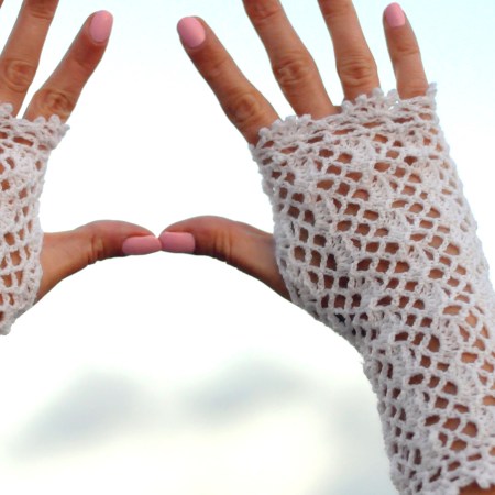 Lace crochet gloves made from white lace weight yarn on a hand, close-up of mesh texture
